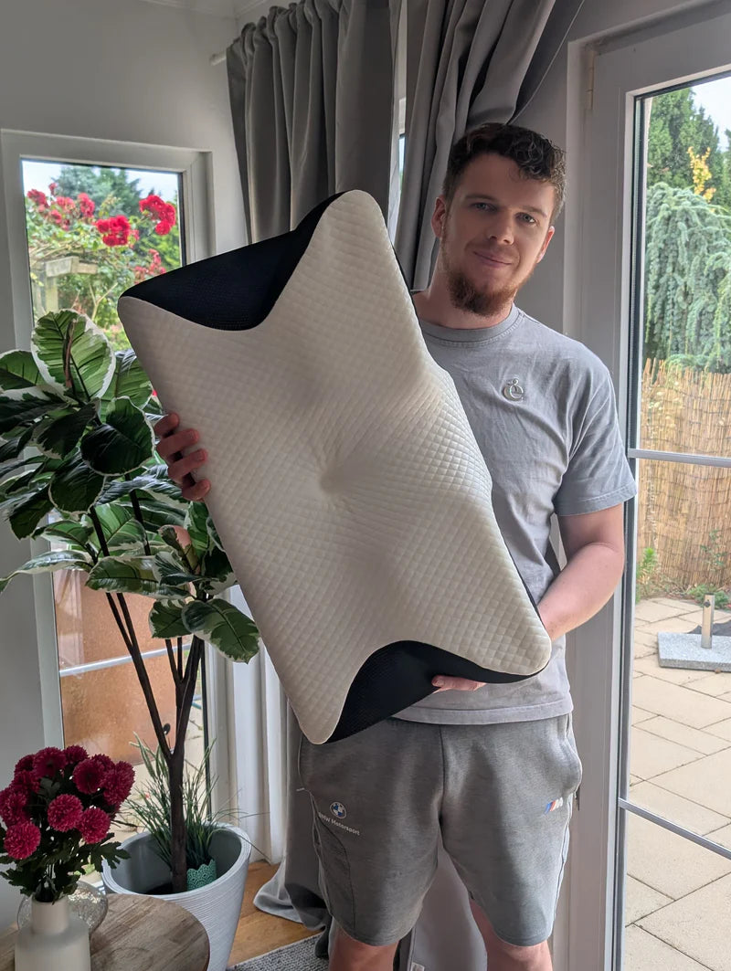 Kundenfoto von Mann mit ergonomischem Nackenkissen in Wohnraum, zeigt Freude und Komfort bei Nackenunterstützung für entspannten Schlaf.